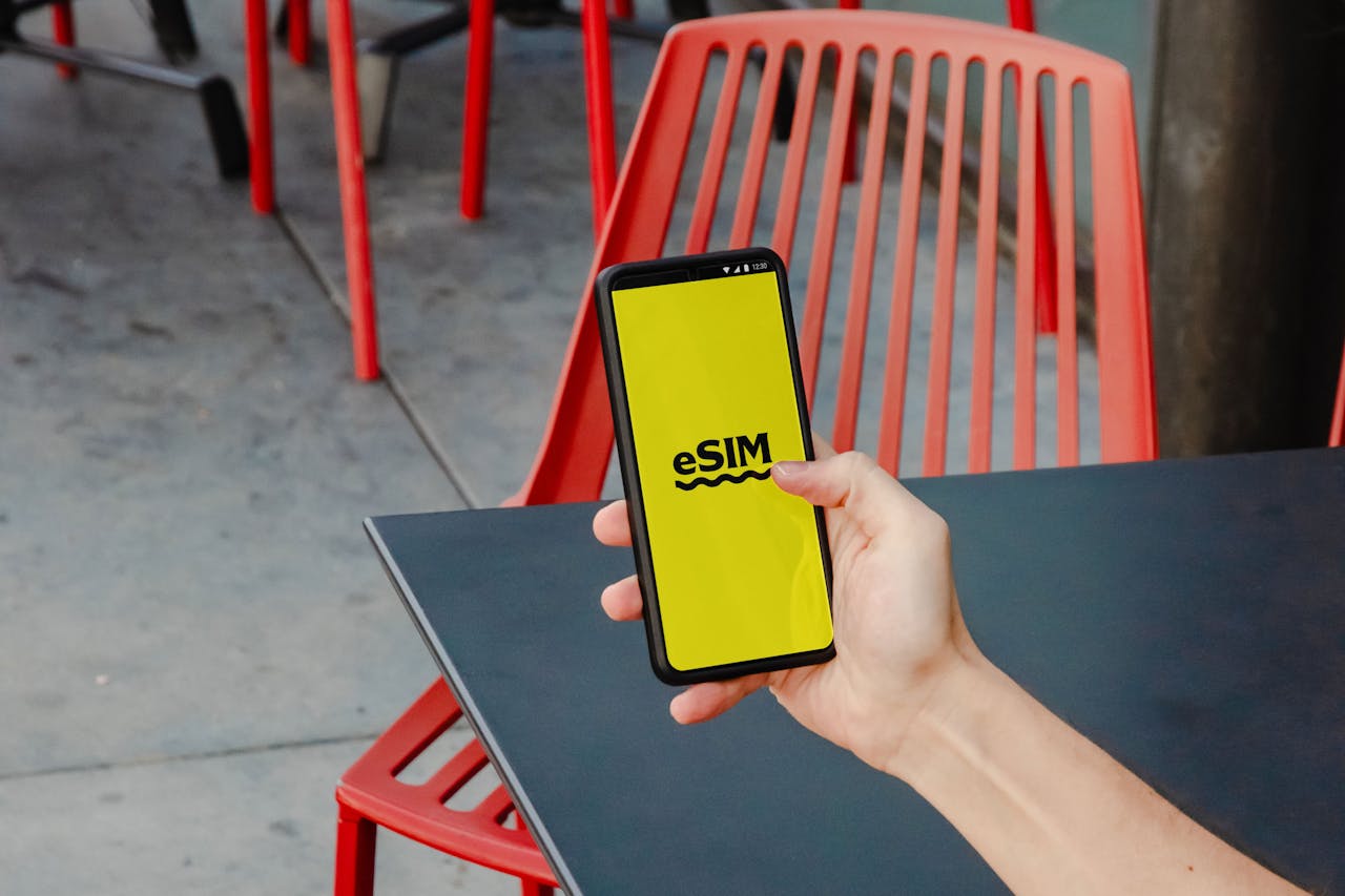 mobile-02 A person holding a smartphone displaying eSIM app screen, outdoors by red chair.